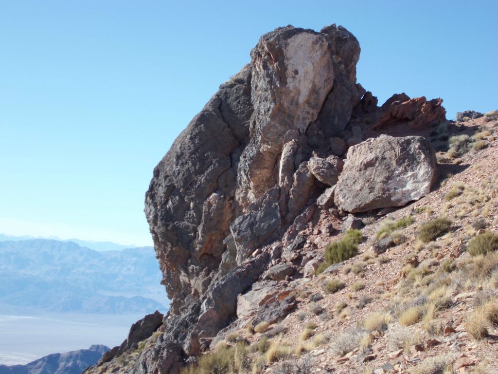 A massive oblong shaped boulder perched on the edge of a cliff: